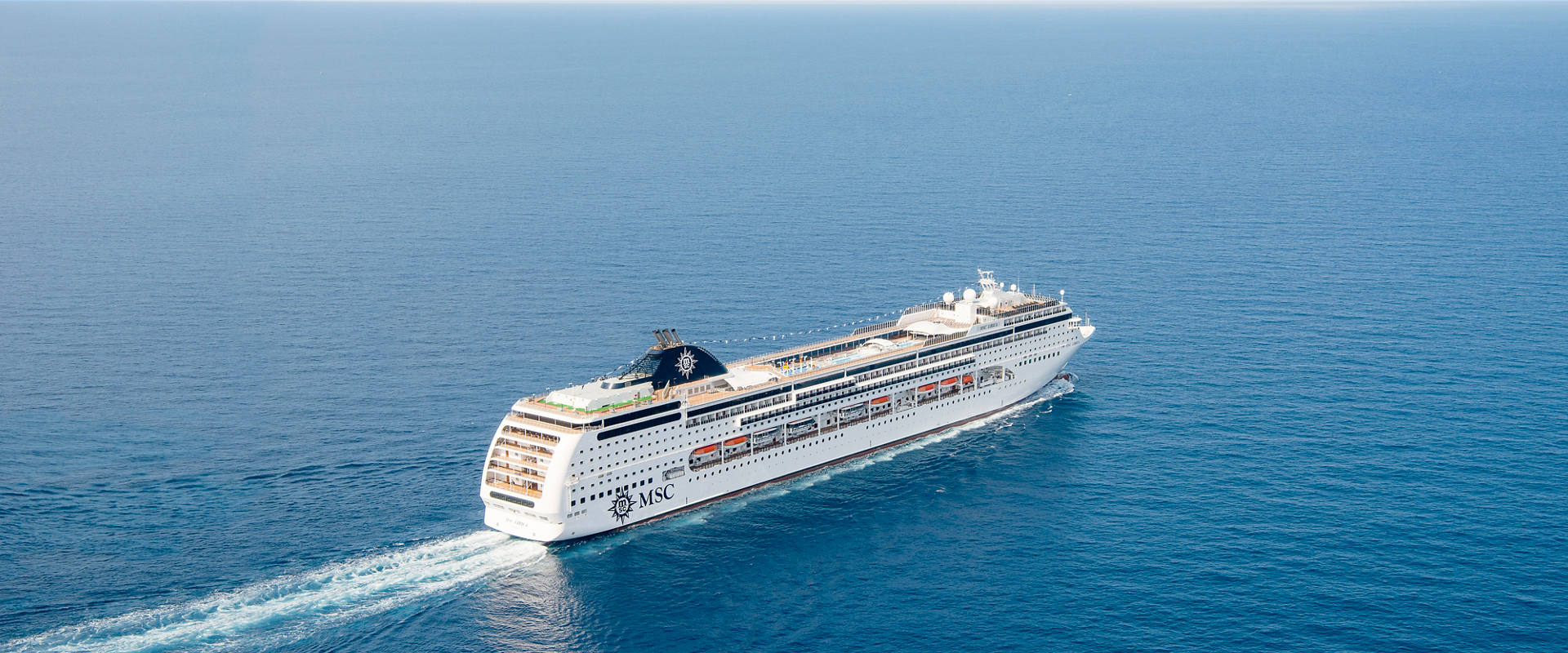 MSC Lirica glides across the deep blue sea under a clear sky with a gentle wake | MSC Cruises