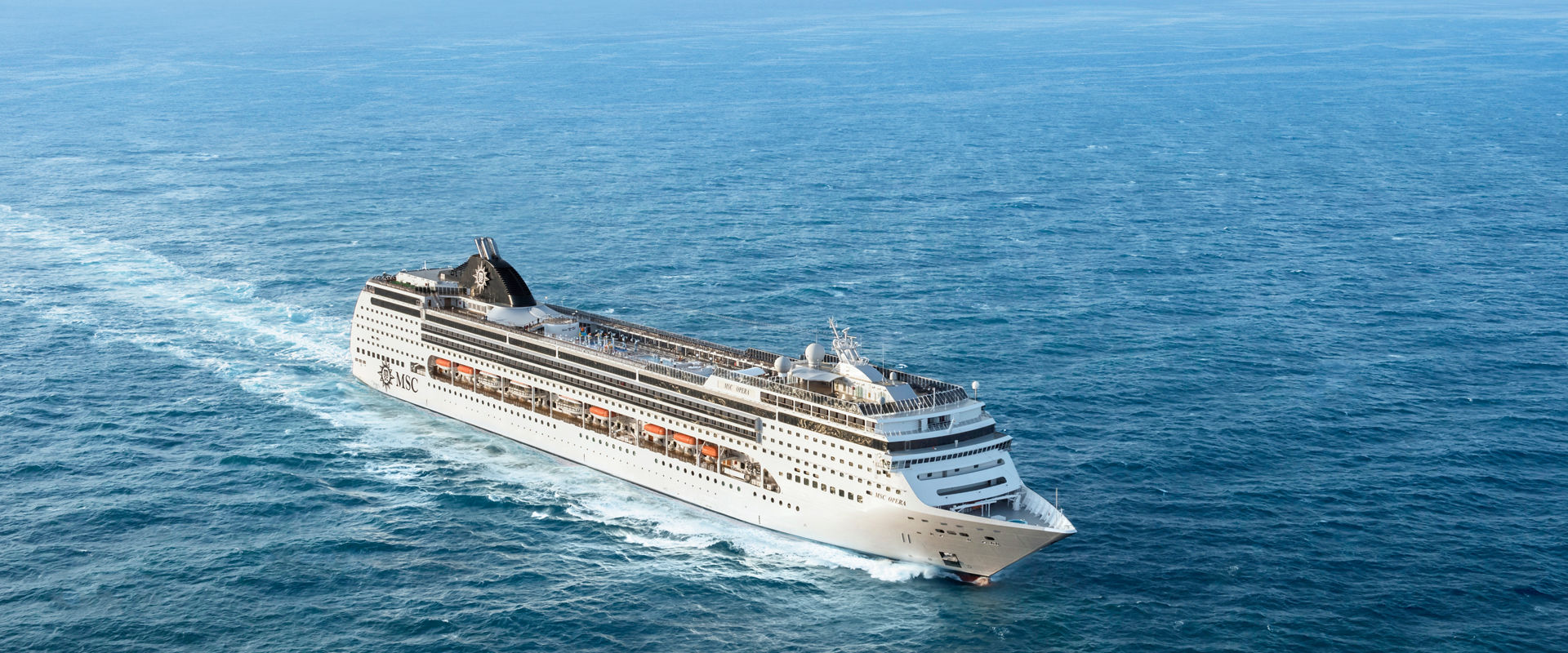 An MSC fleet cruise ship sails across the bright blue sea from an aerial perspective | MSC Cruises
