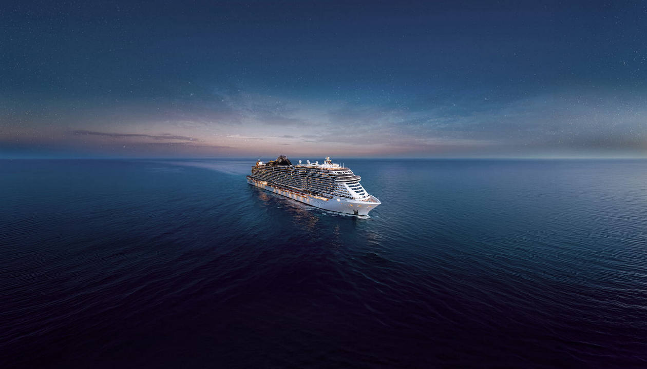 MSC Seashore sails through calm waters at dusk with city lights glowing on the horizon | MSC Cruises