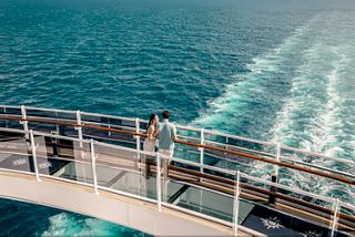 A couple walks across the Bridge of Sighs on MSC Seashore above the blue sea and ship wake foam | MSC Cruises