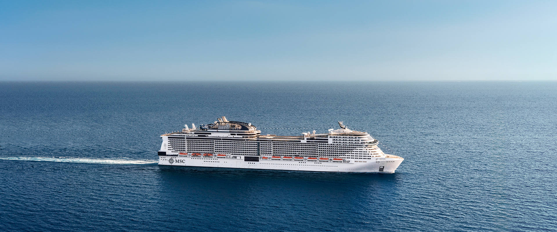 Cruise ship sails across a tranquil blue sea beneath a clear sky | MSC Cruises