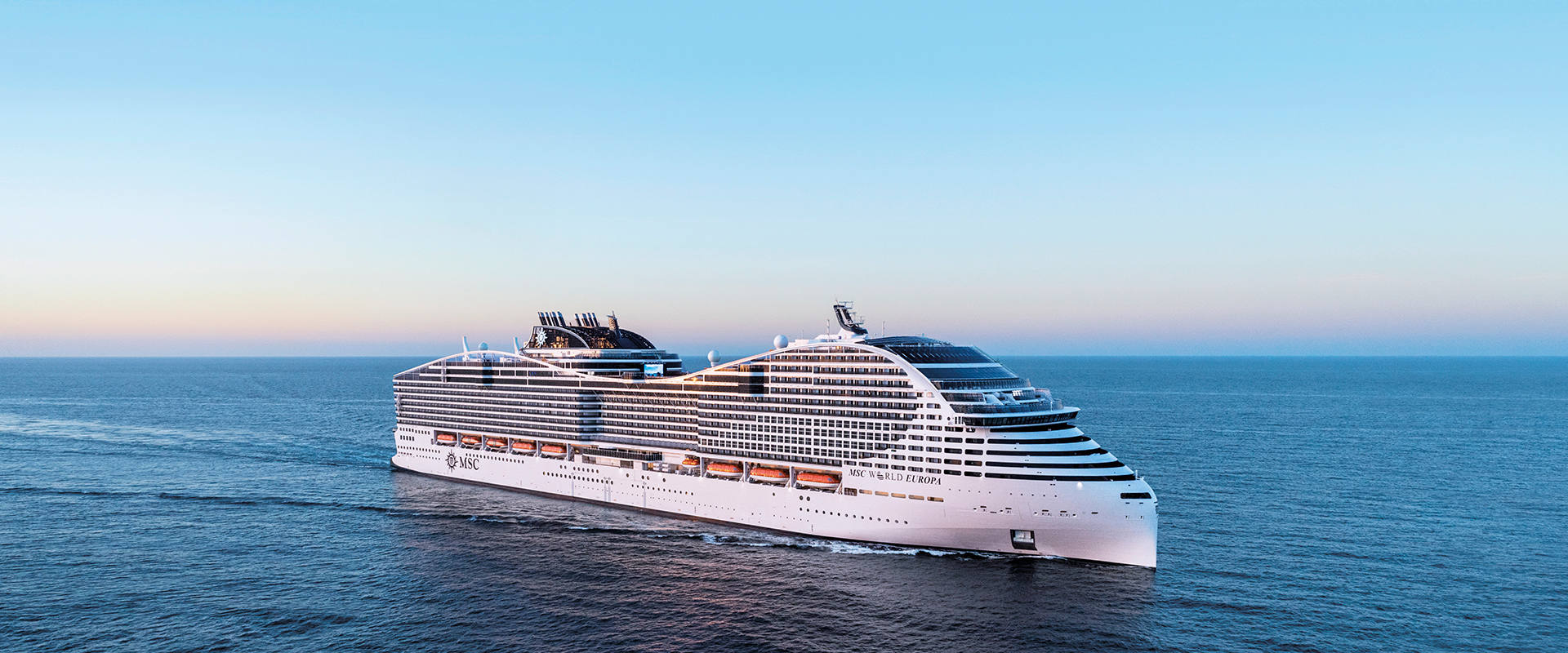 A cruise ship sails across calm waters beneath a clear blue sky | MSC Cruises