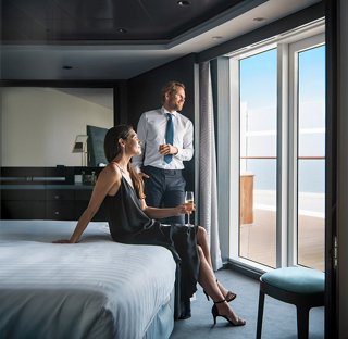 A couple enjoys the ocean view from a spacious suite with floor-to-ceiling windows | MSC Cruises