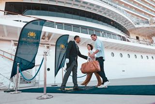 A couple is welcomed by crew with luggage on the blue carpet during MSC Yacht Club embarkation | MSC Cruises