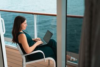 A woman uses a laptop while relaxing on a balcony overlooking the peaceful ocean | MSC Cruises