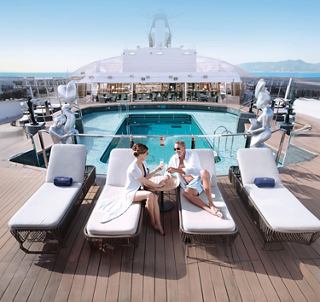 Guests relax on loungers by the pool on the outdoor deck with a panoramic sea view | MSC Cruises