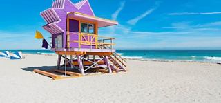 A vibrant lifeguard house stands on sandy beach with blue ocean and clear sky | MSC Cruises