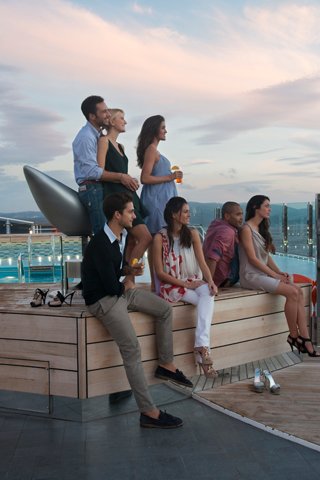 Un groupe divers d'amis profite du temps ensemble au bord de la piscine sur le MSC Divina, avec un magnifique coucher de soleil en arrière-plan | MSC Croisières