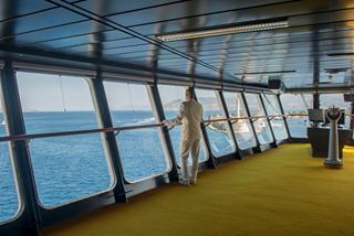Un ufficiale navale è in piedi sul ponte di comando, osservando il mare sereno attraverso ampie finestre | MSC Crociere