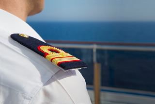 A naval officer in uniform stands confidently on the ship's deck with the sea in the background | MSC Cruises