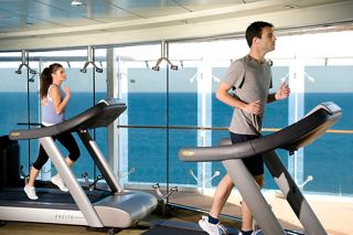 Una pareja se ejercita en cintas de correr en un gimnasio luminoso con vistas al océano, promoviendo el fitness y el bienestar a bordo | MSC Cruceros