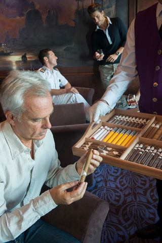 A naval officer engaging with guests at a bar while enjoying a cigar on board MSC Divina | MSC Cruises