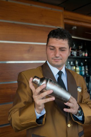 A bartender in a stylish brown jacket prepares a cocktail with a shaker at the bar on MSC Splendida | MSC Cruises