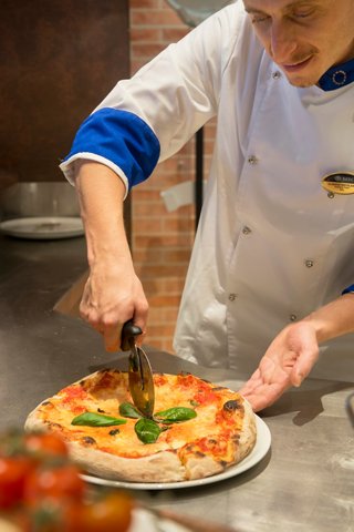 A skilled chef prepares a delicious pizza with fresh ingredients in La Cantina Di Bacco on MSC Divina | MSC Cruises