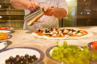 Ein Koch bereitet gekonnt eine köstliche Pizza mit frischen Zutaten in einem lebhaften Restaurant zu | MSC Cruises