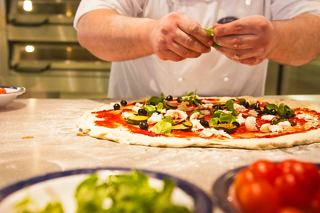 A chef skilfully prepares a pizza by adding fresh basil to the toppings | MSC Cruises