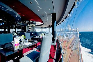 Un elegante comedor a bordo del MSC Divina, con mesas y sillas con vista al mar a través de grandes ventanas | MSC Cruceros