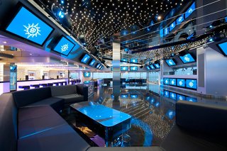 A vibrant disco area on MSC Magnifica featuring a bar counter, seating, and screens for entertainment | MSC Cruises