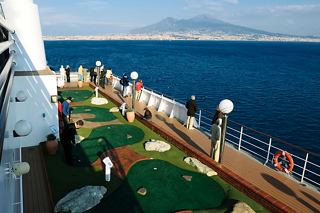 Guests enjoy a sunny day playing mini-golf on the deck of MSC Musica with the sea and coast in the background | MSC Cruises