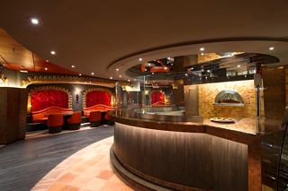 A welcoming interior of La Locanda restaurant featuring a curved bar and seating area for enjoying delicious pizza | MSC Cruises