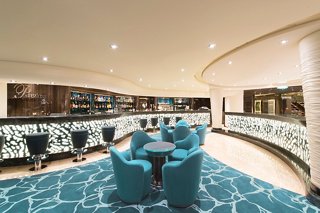 A stylish bar area featuring comfortable turquoise armchairs, a sleek bar counter, and an inviting atmosphere | MSC Cruises