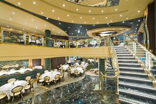 An elegant dining area featuring tables set with cutlery and flowers, complemented by a grand staircase and warm decor | MSC Cruises