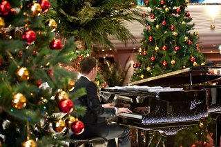 Un talentoso músico toca el piano rodeado de decoraciones navideñas festivas en un cálido área de recepción | MSC Cruceros