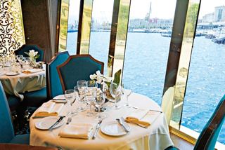 A beautifully set dining table beside large windows offering a scenic view of the water | MSC Cruises