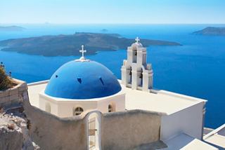 A serene view of a blue-domed church overlooking the tranquil sea in Santorini, Greece | MSC Cruises