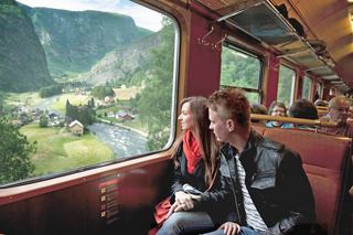 A couple enjoys a scenic train excursion through the beautiful Norwegian landscape, with lush greenery and a river visible | MSC Cruises