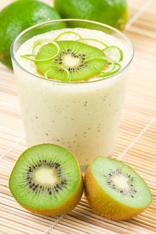 A refreshing kiwi milkshake in a glass, garnished with lime, sits beside sliced kiwi on a wooden surface | MSC Cruises