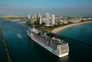 The MSC Divina ship sails through a bay with skyscrapers in the background | MSC Cruises