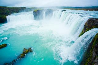 A stunning view of Godafoss waterfall cascading into a turquoise pool, surrounded by rugged rocks and natural beauty | MSC Cruises