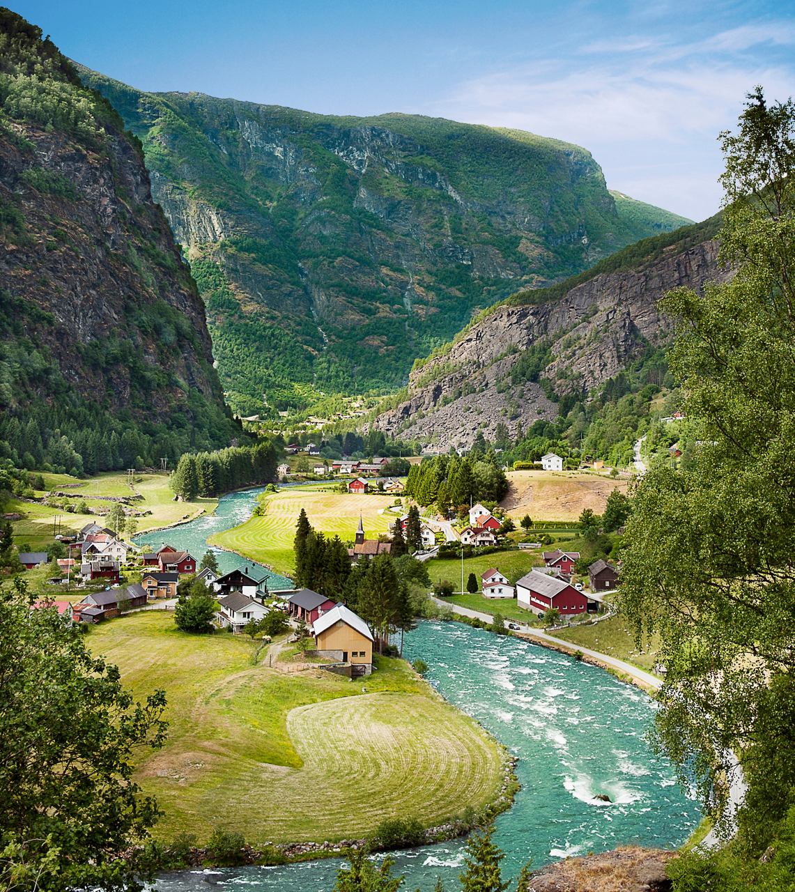 Una vista serena di Flaam, Norvegia, con un fiume che serpeggia tra colline verdi e case pittoresche nella valle | MSC Crociere
