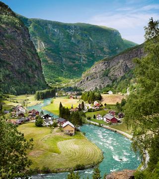 Una vista serena di Flaam, Norvegia, con un fiume che serpeggia tra colline verdi e case pittoresche nella valle | MSC Crociere
