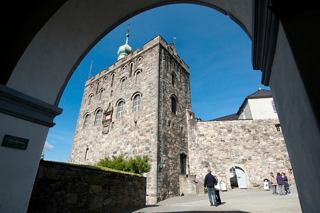 A historic building in Bergen framed by an archway, with people walking and a clear blue sky above | MSC Cruises