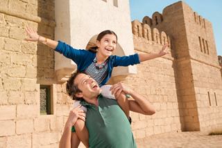 A father joyfully carries his child on his shoulders near a historic wall in Tunisia | MSC Cruises