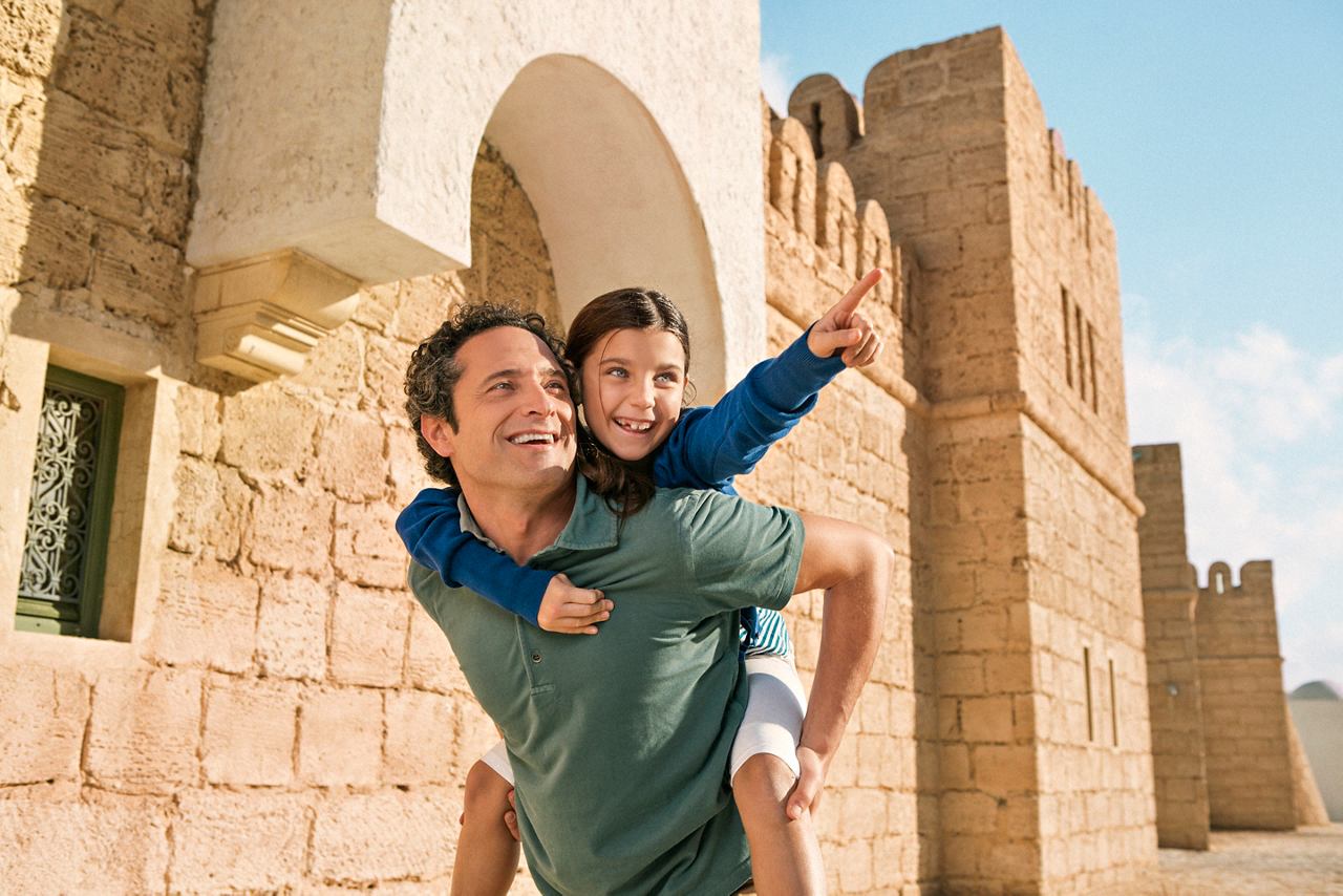 Un père porte son enfant sur le dos, profitant d'une excursion près d'un mur ancien en Tunisie | MSC Cruises