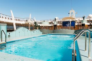 Ein erfrischender Swimmingpool, umgeben von Sonnenliegen auf dem Deck der MSC Preziosa unter einem klaren blauen Himmel | MSC Cruises