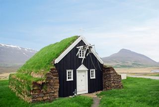 A charming grass-roofed house nestled in the stunning landscapes of Akureyri, Iceland, with mountains in the background | MSC Cruises