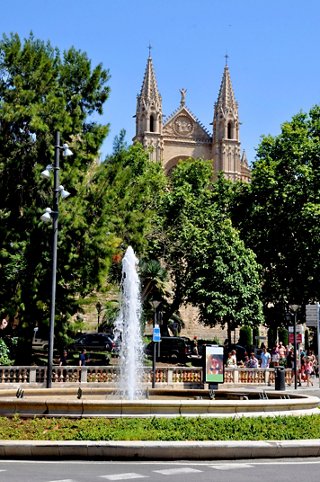 Una vista escénica de una iglesia histórica rodeada de árboles frondosos y una fuente en Palma de Mallorca | MSC Cruceros