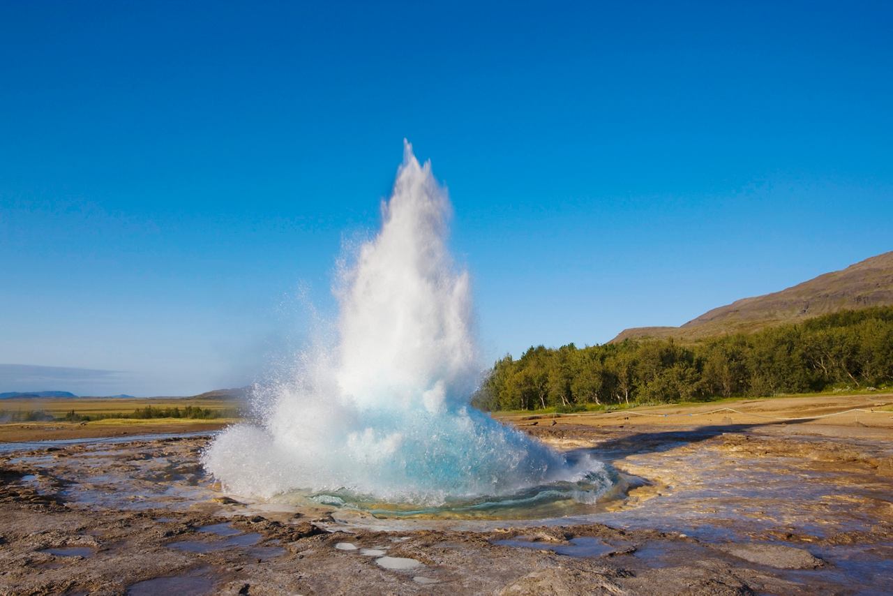 A geyser erupts with a powerful burst of water against a clear blue sky in Iceland's stunning landscape | MSC Cruises