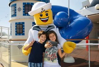 Two children happily pose with a large Lego character in a vibrant children's entertainment area | MSC Cruises