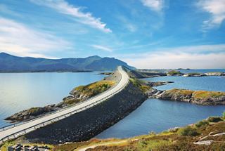 A scenic view of a winding road along the coastline of Norway, surrounded by mountains and sea | MSC Cruises