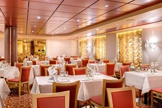 Elegant dining area with tables set for guests, featuring warm lighting and inviting décor | MSC Cruises