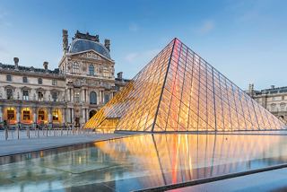 The illuminated glass pyramid of the Louvre Museum stands majestically at sunset in Paris | MSC Cruises