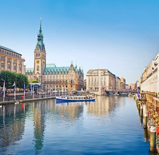 Una vista serena del Ayuntamiento de Hamburgo reflejada en el tranquilo río, invitando a explorar este vibrante destino | MSC Cruceros