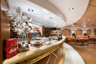 A stylish bar area featuring a warm ambiance, coffee, and cake offerings for guests to enjoy | MSC Cruises