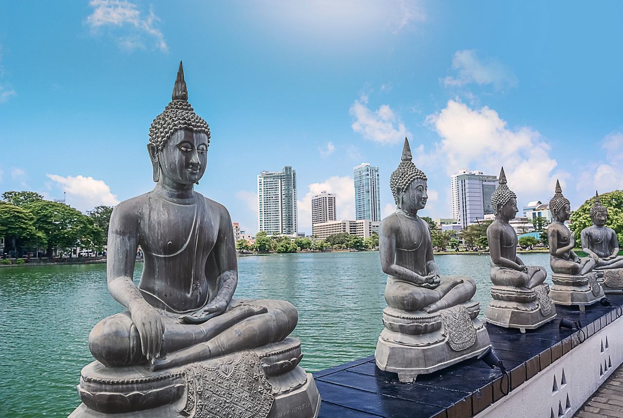 Buddha statues lined along a serene lake with a vibrant city skyline in the background | MSC Cruises