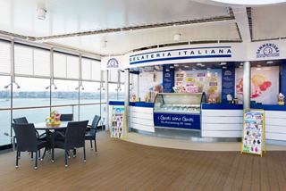 A welcoming lounge area with tables and chairs, featuring a gelateria and large windows overlooking the sea | MSC Cruises